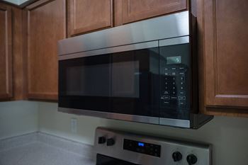 A black microwave oven with a digital display is mounted on a kitchen wall above a stainless steel stove.